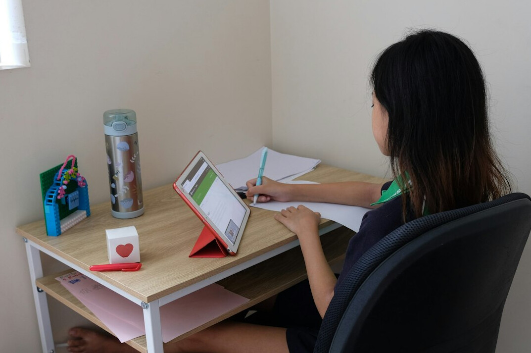 Researcher writing notes while reviewing statistical charts on a laptop screen